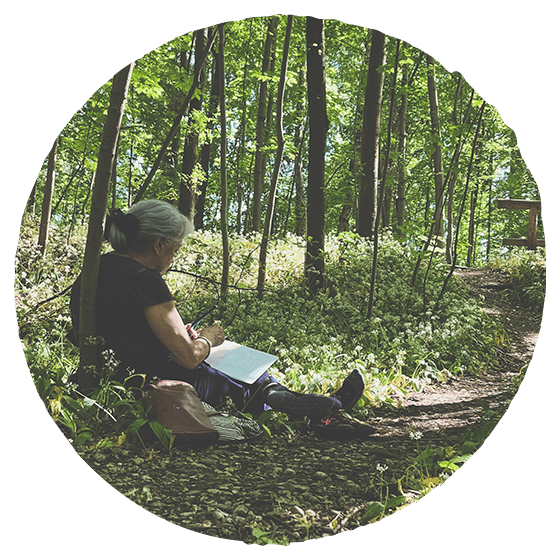Naturhalt Waldbaden: Eine Frau sitzt entspannt am Waldboden und zeichnet eine Hörkarte – welche Geräusche nimmt sie in der Natur wahr