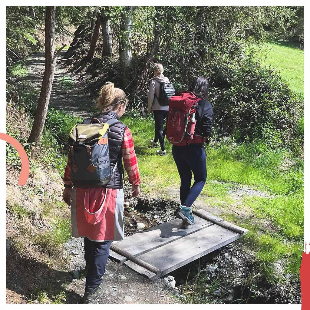 Naturhalt Achtsamkeits-Workshop: 3 Frauen* gehen über eine kleine Brücke in der Natur bei Sonnenschein